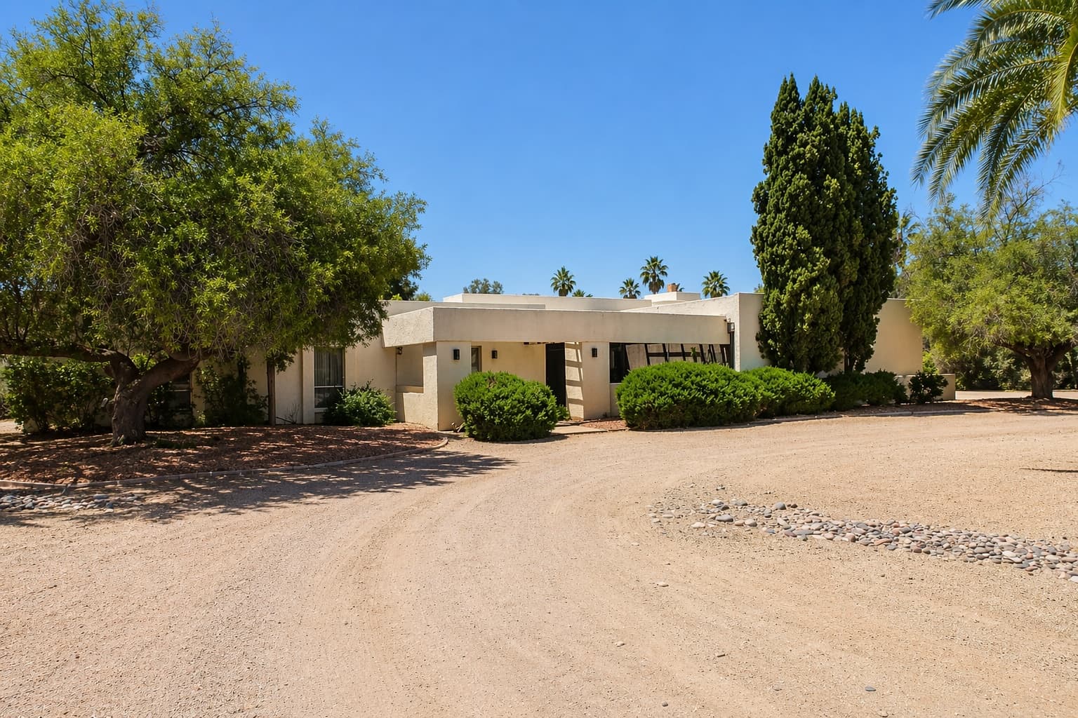 Single-level Southwestern home set back behind a circular drive lined with mature desert trees.