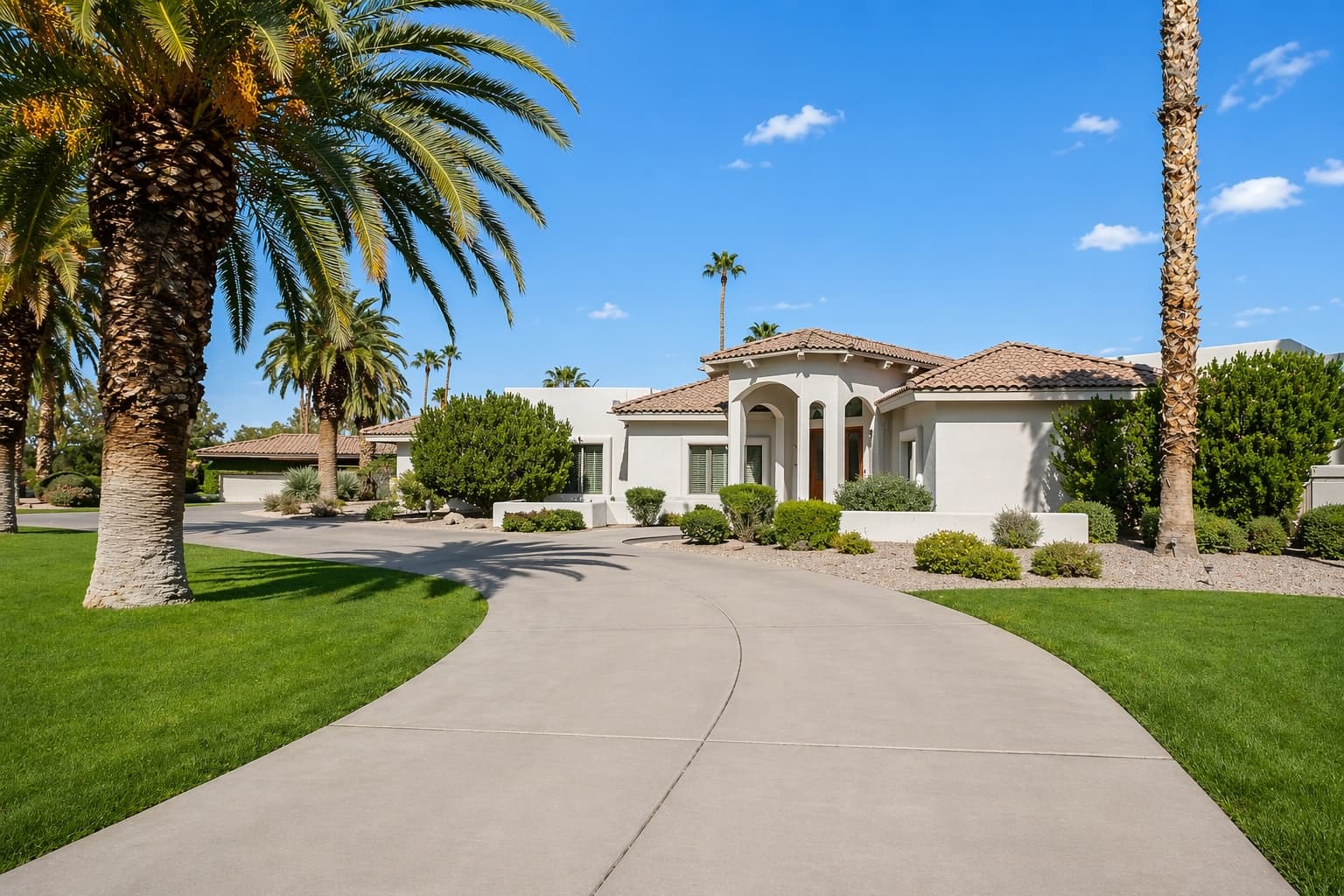 Mediterranean-style home with terracotta roof and a curved drive flanked by mature palms.